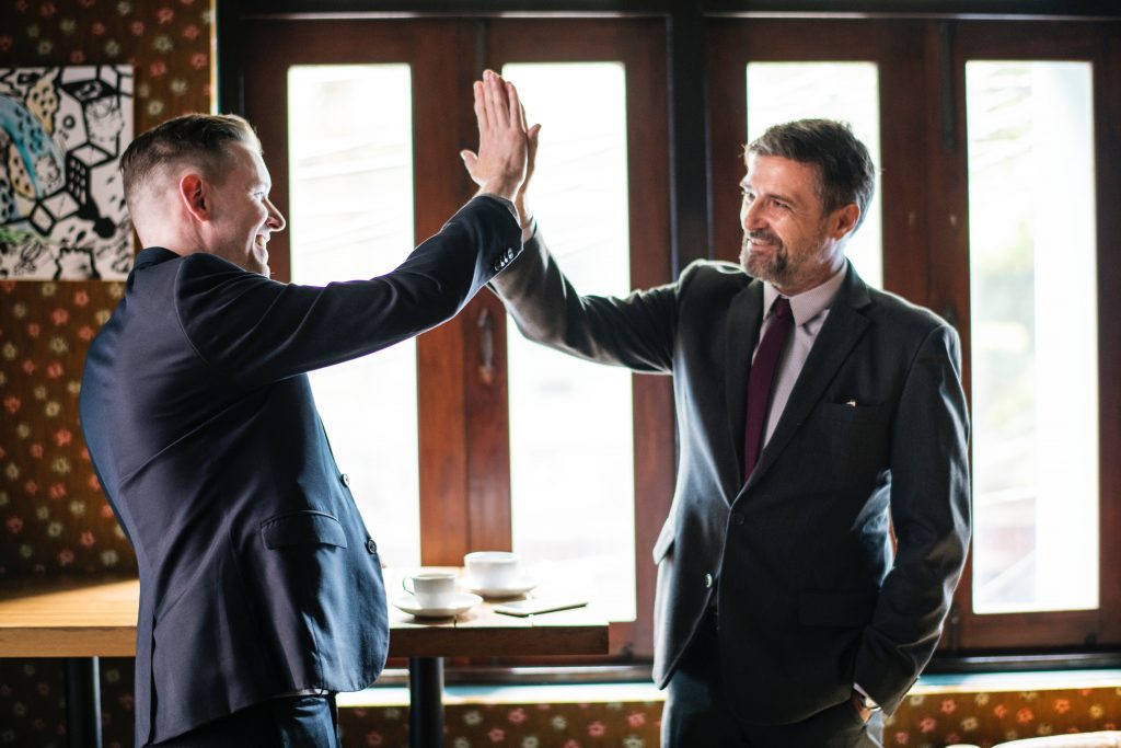 Two businessmen high-fiving in a successful meeting with coffee on the table.