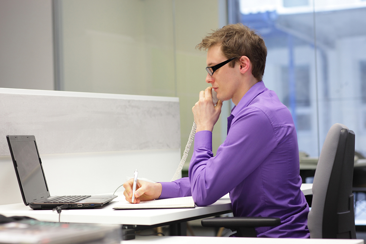 Focused professional in a purple shirt working intently at his desk with a laptop.
