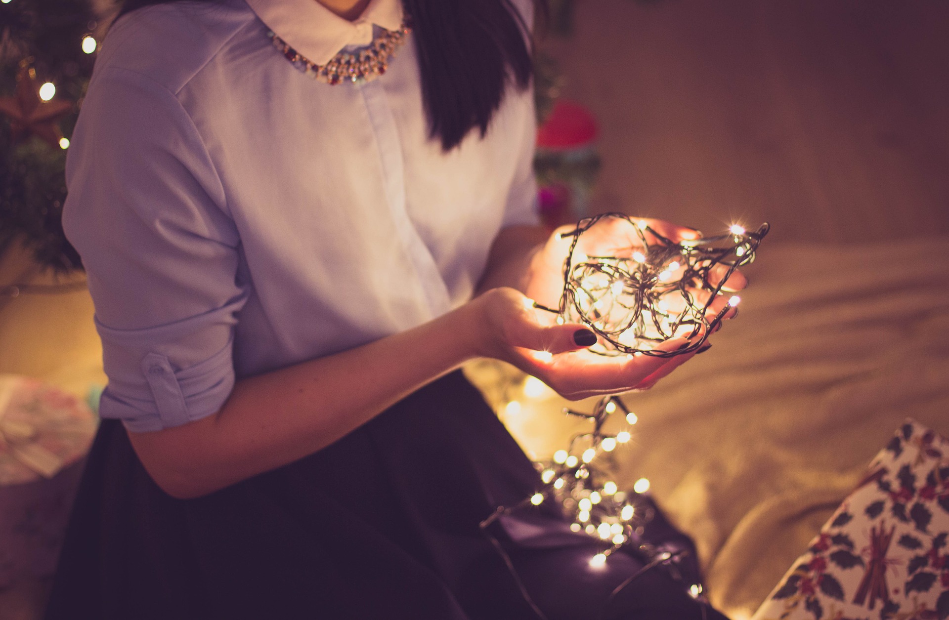 Woman in a light blue shirt holding a bundle of holiday string lights.