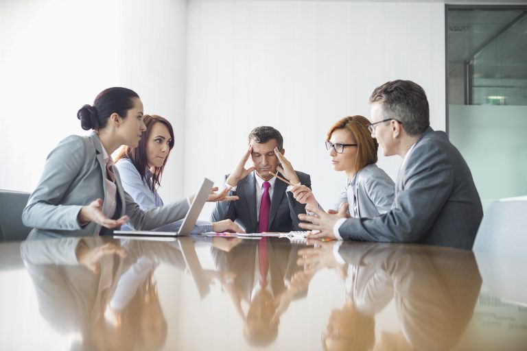 Stressed businessman surrounded by colleagues in a tense meeting.
