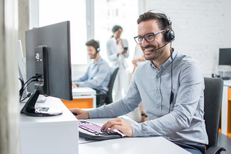 Smiling customer service representative wearing a headset and working at a computer in an office.