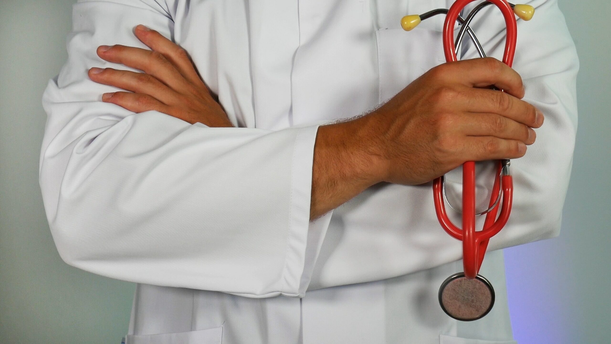 Doctor in a white coat holding a red stethoscope with arms crossed.