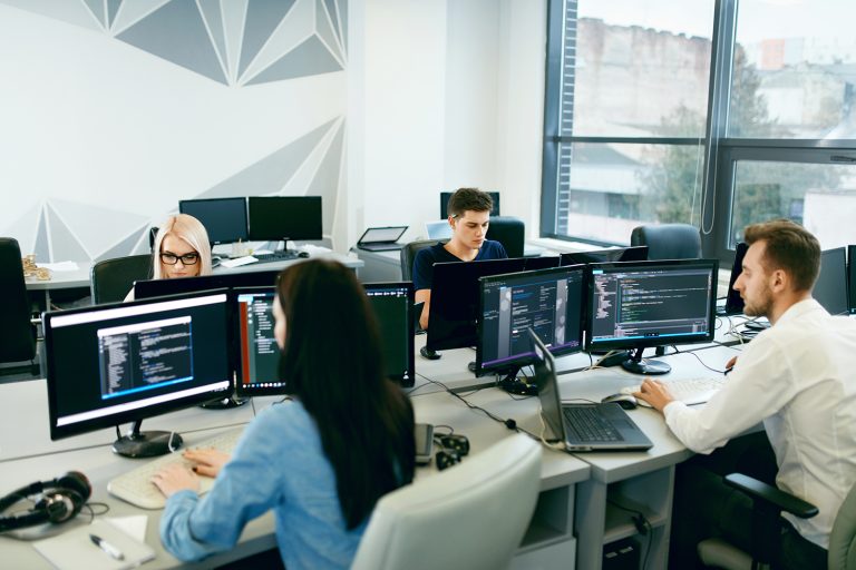 Group of focused programmers working on multiple computer screens in a modern office.