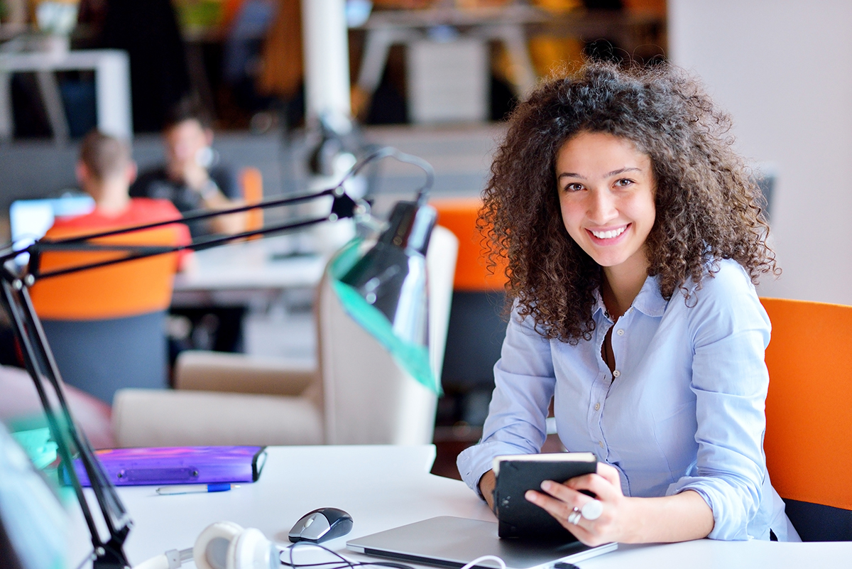 Smiling young woman with curly hair using tablet in a busy modern office.