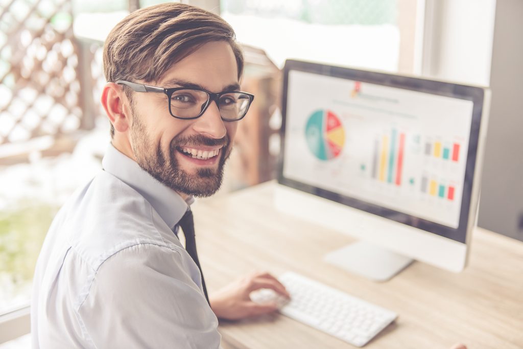 Smiling man with glasses working on computer displaying charts and graphs.